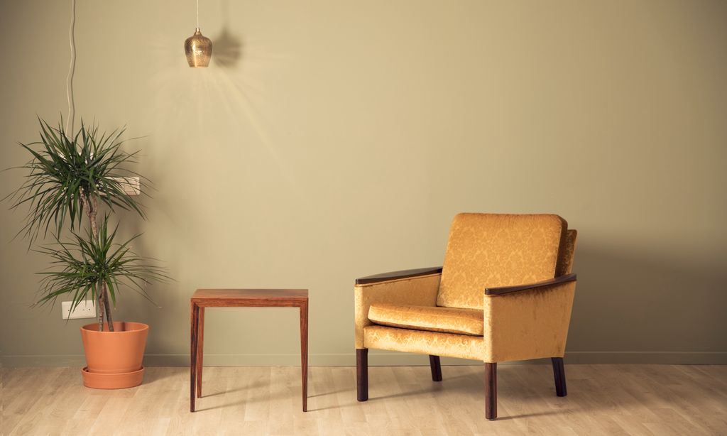 Mønstrete gul retrostol står ved siden av et lite bord og en potteplante. Foto.