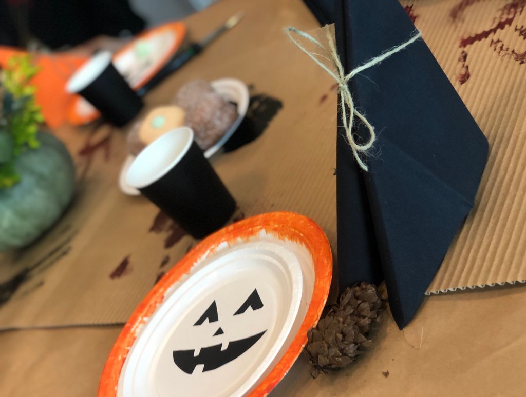 Et bord som er dekt til halloween-fest, med svarte servietter og papirkopper, og hvite papirtallerkener som er dekorert med oransje og svart. Foto.