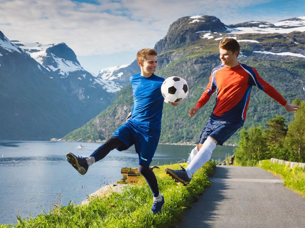 To personar svevar i lufta med ein fotball i eit fjordlandskap. Ansikta er fordreidde og har utydelege detaljar. Eit bein har ein unaturleg vinkel. KI-foto.