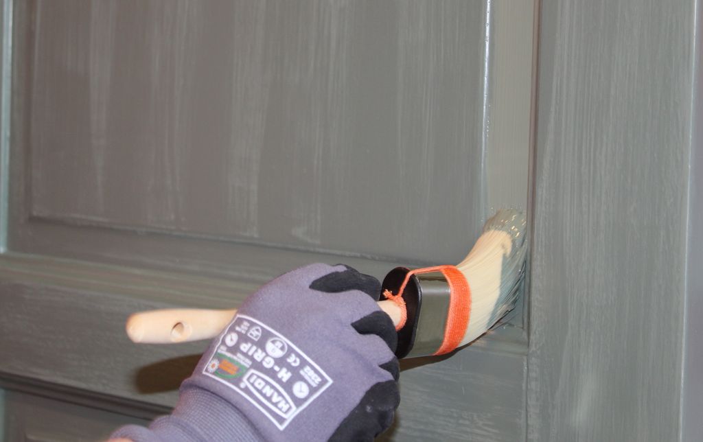 Grå maling påføres en dør med pensel. Foto.