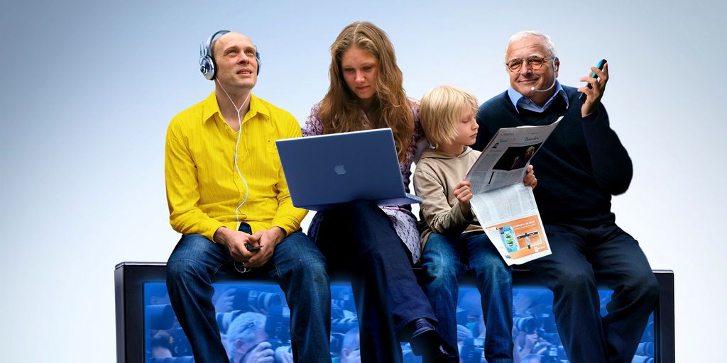 Fire personer i ulike aldre sitter på et TV-apparat med avis, lydavspiller, PC og mobil. Foto.