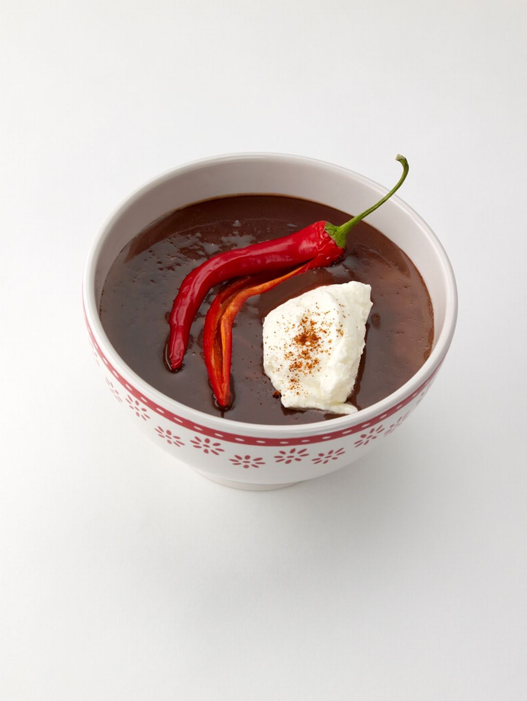 Kopp med brunt drikke. Oppi drikken er det en rød chili og en klump hvit krem med et dryss av brunt krydder. Foto.