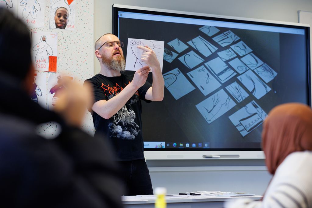 Mann står ved digital tavle og demonstrerer for elever hvordan han jobber. Foto.