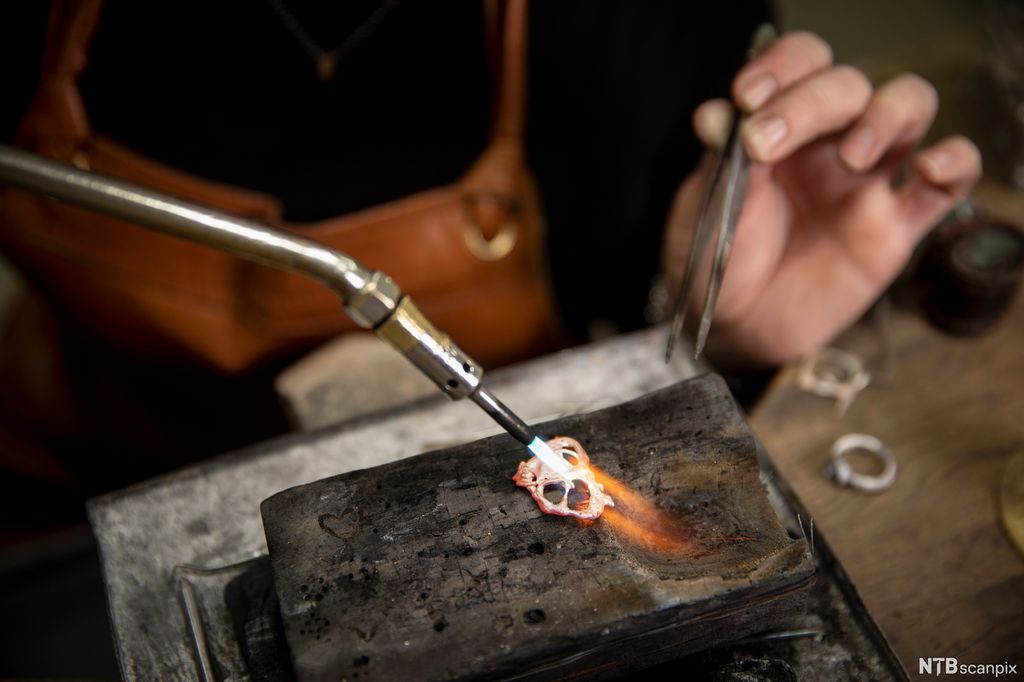 Gullsmed loddar eit metallarbeid. Foto.