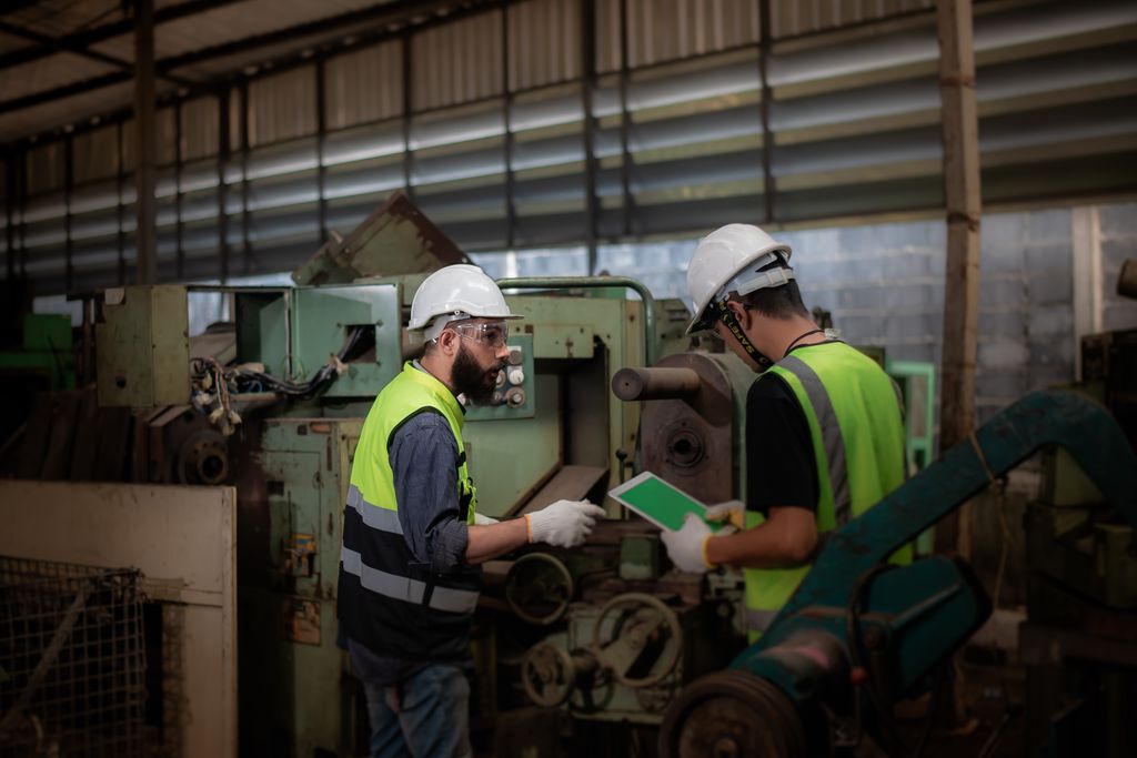 To unge teknikere med hjelm og arbeidstøy inspiserer et anlegg i en fabrikk. Foto.