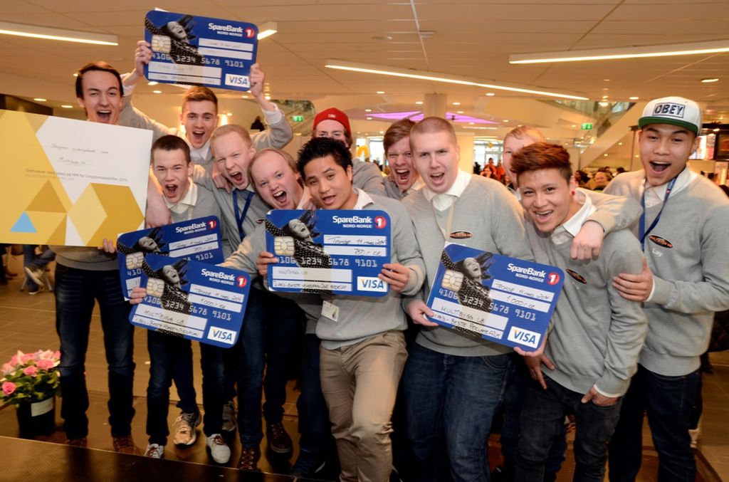 Et titalls glade, ropende ungdommer. De holder plakater utformet som kredittkort med navn og pengesummer på. Foto.