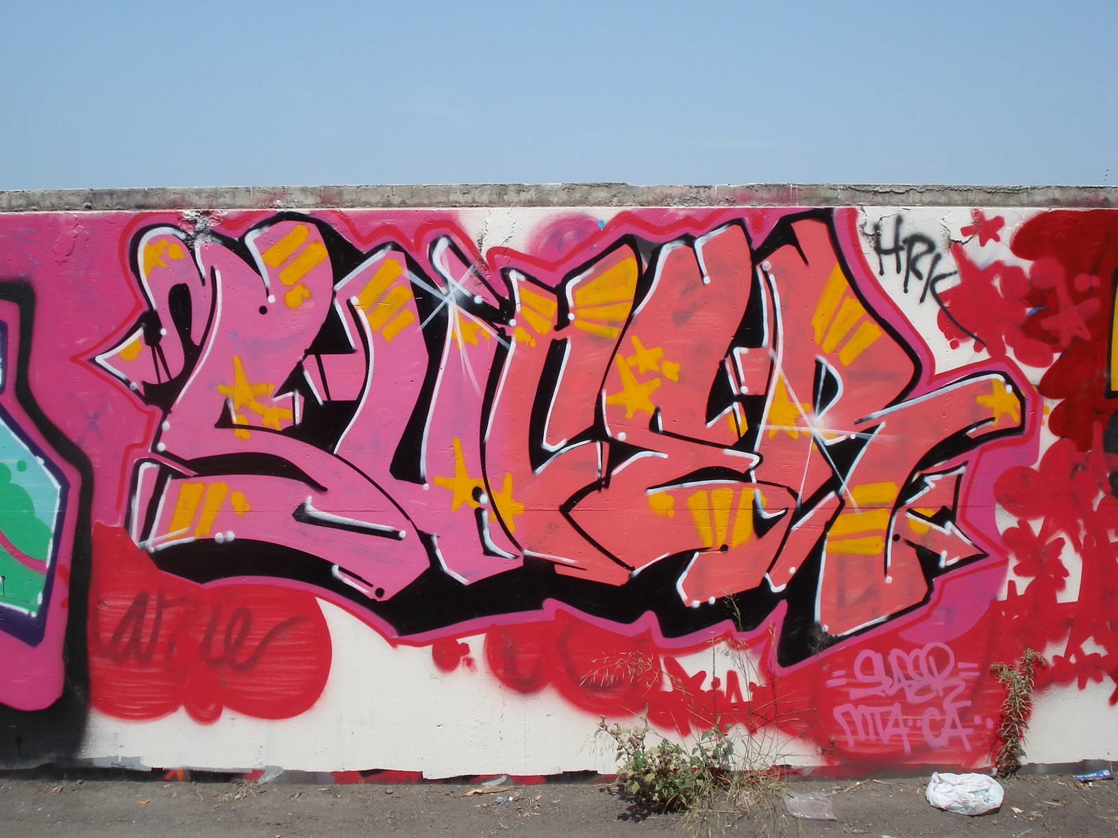 Rødrosa graffitibokstaver på en hvit vegg. Foto.