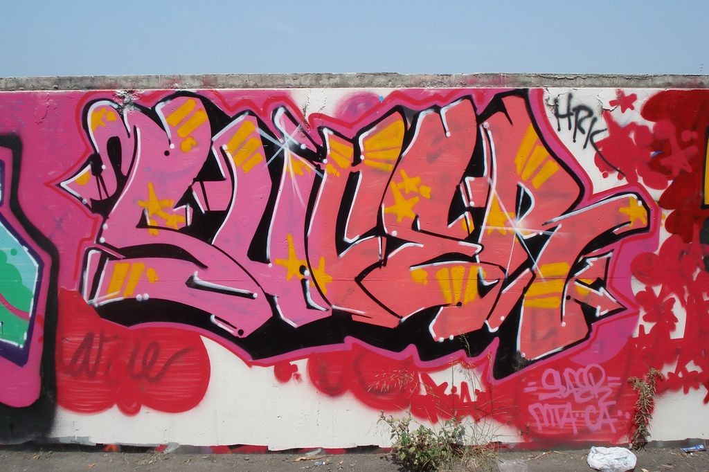 Rødrosa graffitibokstaver på en hvit vegg. Foto.