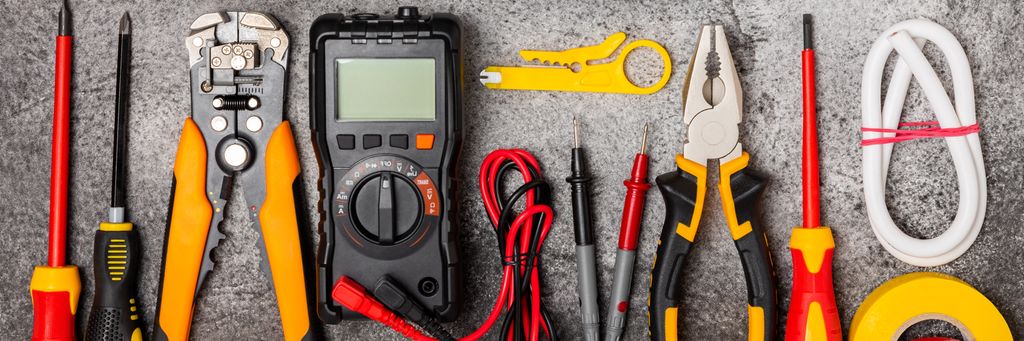 Multimeter, konstruksjonsteip, elektrisk teip, skrutrekkere, tang, automatisk isolasjonsstripper, stikkontakt og LED-lampe. Foto.