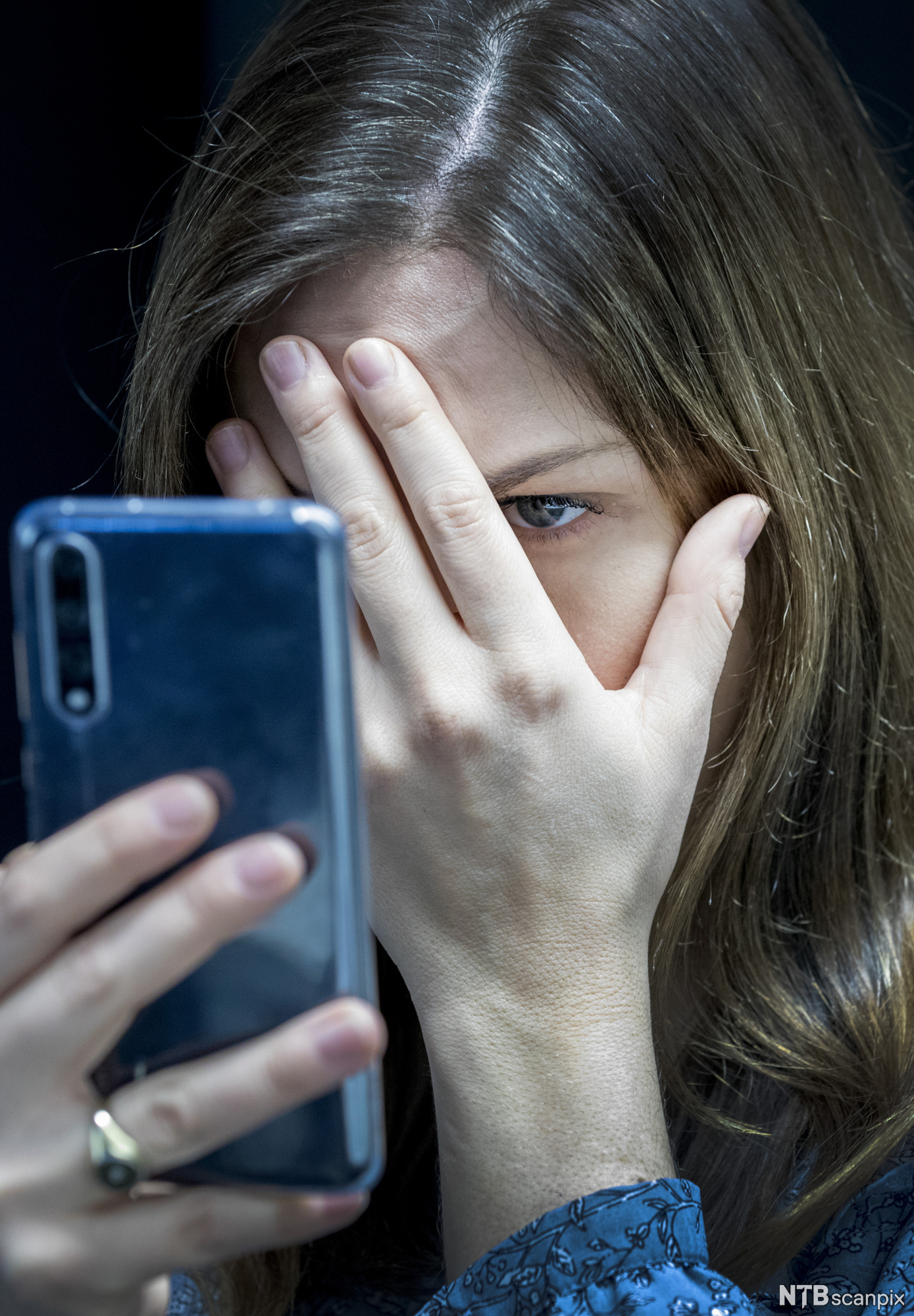 Kvinne les hatefulle ytringar på mobiltelefon og held handa framfor halve ansiktet. Foto.