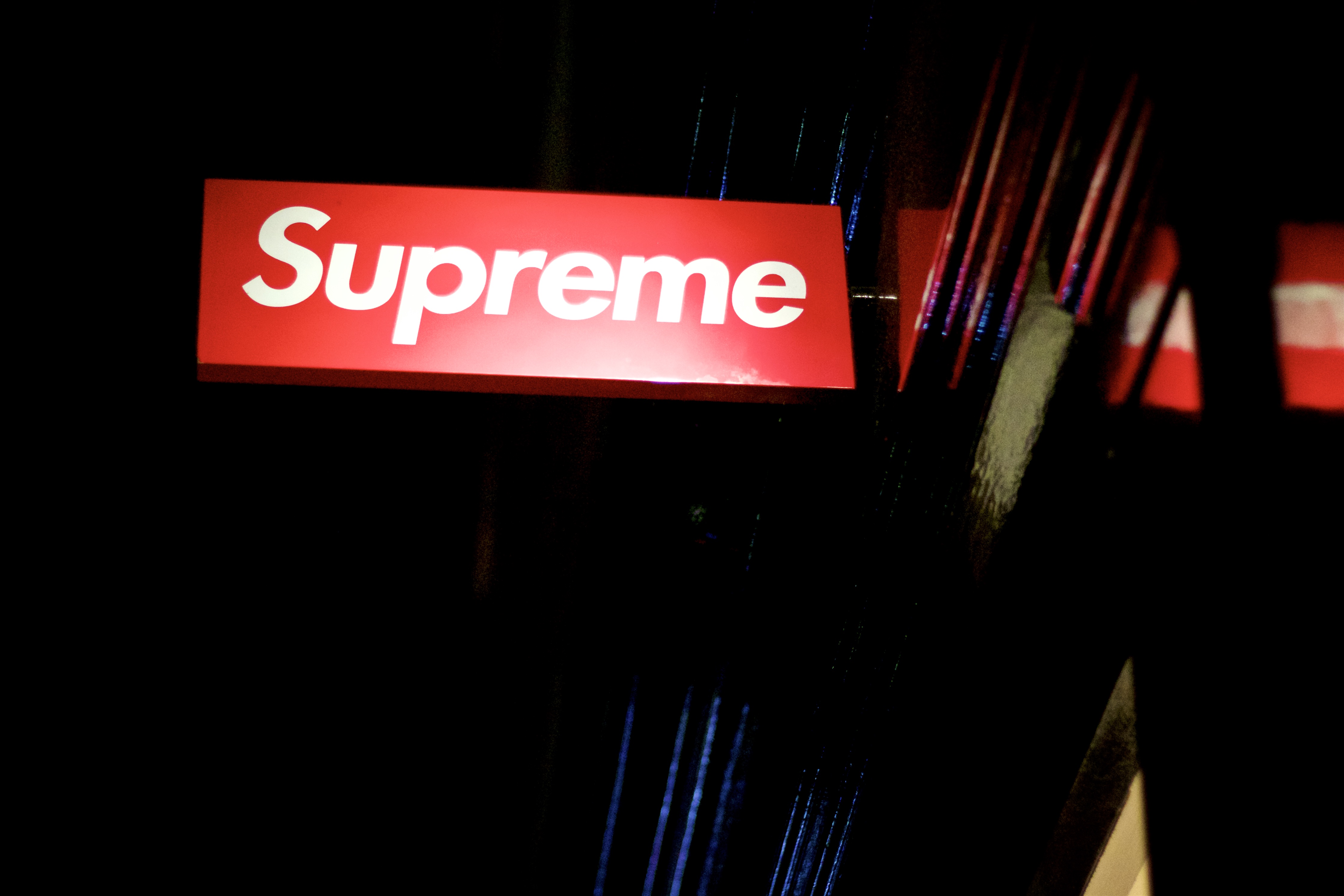 Butikkskilt med teksten "Supreme". Rød bakgrunn med hvit skrift. Foto.