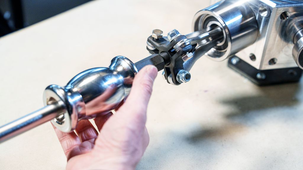 Ei hånd som holder et sylindrisk verktøy med tre bein festet i et lager. Foto.