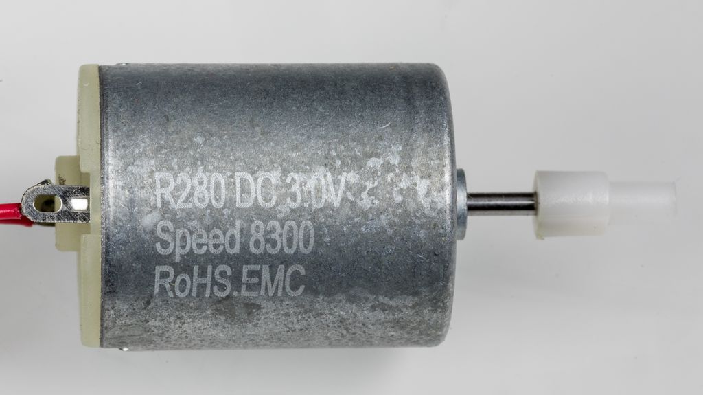 DC-motor med tilkoplingsledninger på venstre side og ei utstikkende aksling på høyre side. Motoren har påskrifta R280 DC 3.0V, Speed 8300 og RoHS.EMC. Foto.
