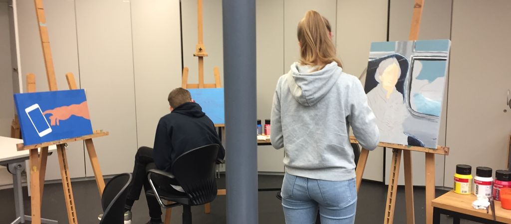 To elever jobber med malerier som står på staffeli. Foto.