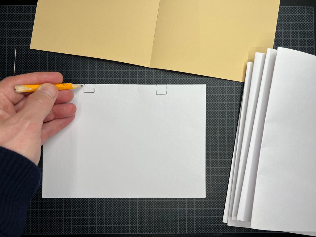 Ei hånd holder en blyant og markerer bredden på stiftene. Foto.