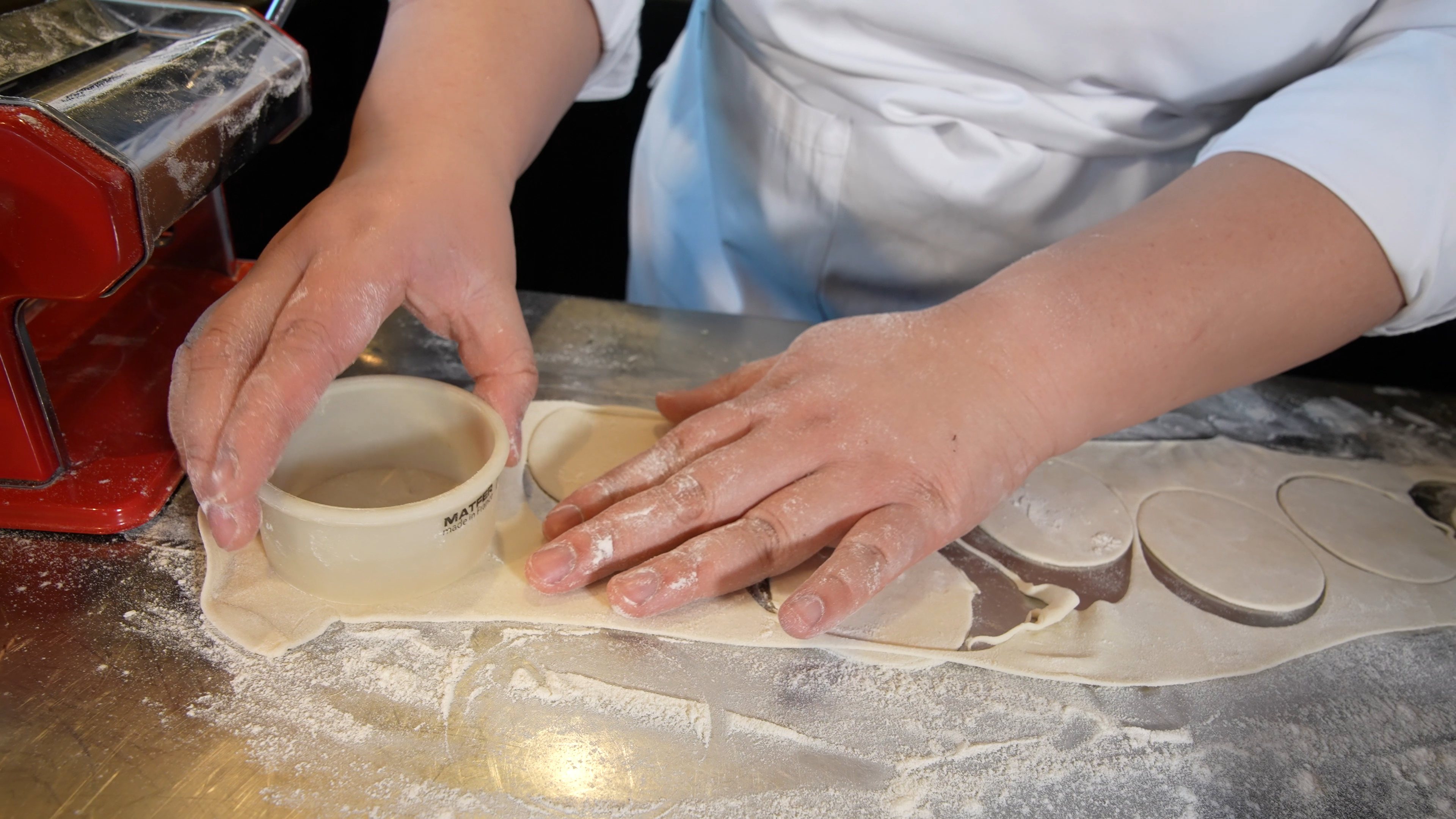 Nærbilde av tynn deig med mel rundt, en person bruker en utstikker til å stikke ut sirkler. Foto.