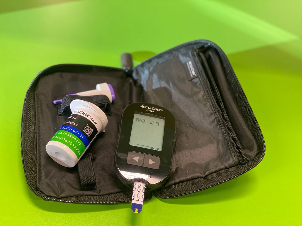 En sort, digital blodsukkermåler som ligger i en liten sort mappe på et grønt bord. Foto.