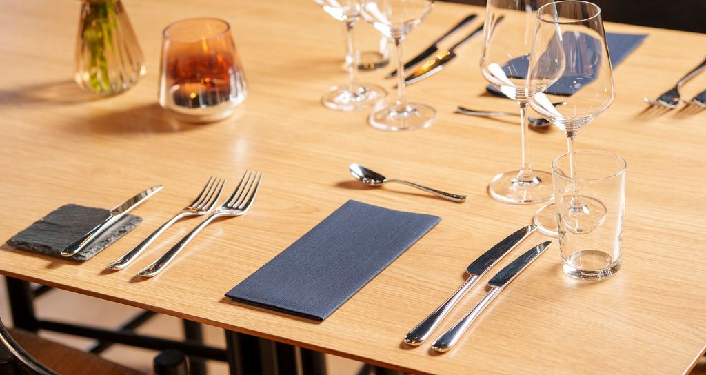 Eit dekt bord i ein restaurant. På bordet er det smørekniv, forrettsbestikk, hovudrettsbestikk, dessertskei, vinglas, vassglas og serviett. Foto.