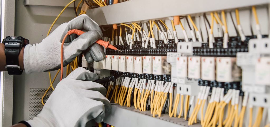 En fagperson med isolerhansker tester elektriske installasjoner og ledninger på et relébeskyttelsessystem. Foto.