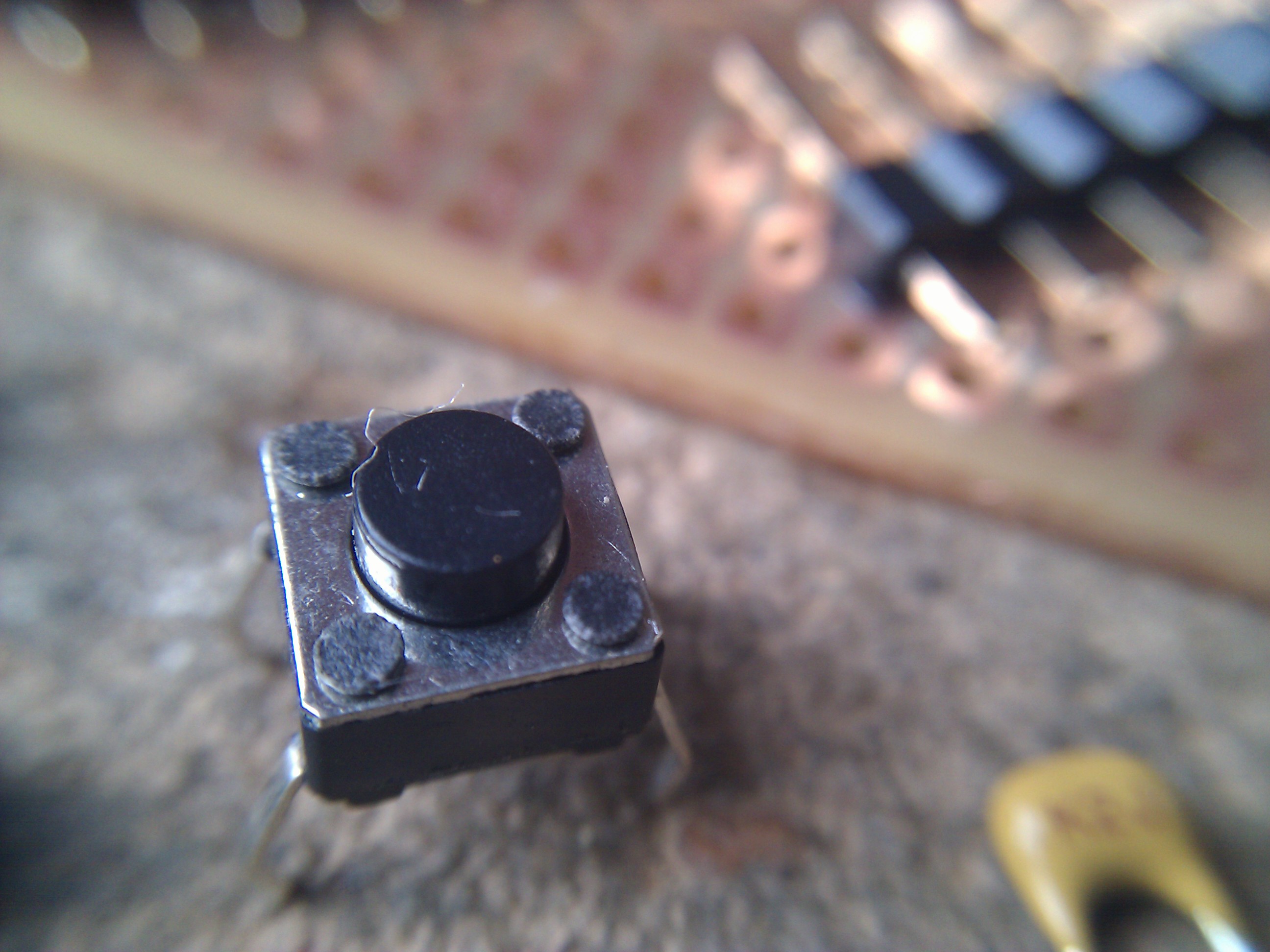 Svart trykknapp med fire tilkoblingspunkter. Foto.