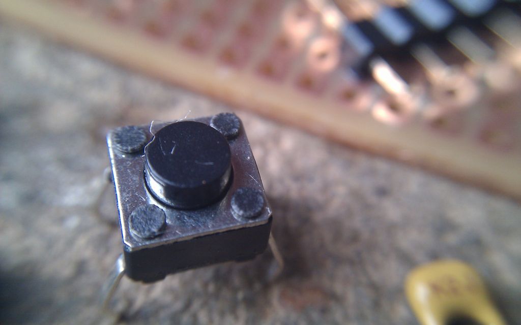 Svart trykknapp med fire tilkoblingspunkter. Foto.