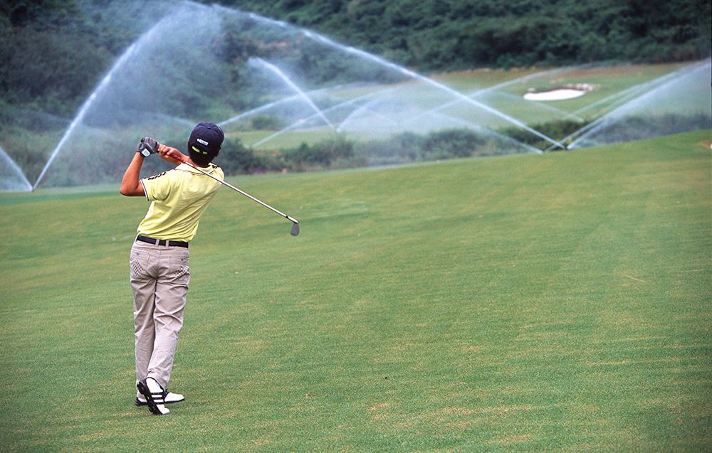 Vannstråler og golfspiller som nettopp har slått en ball på golfbane. Foto.