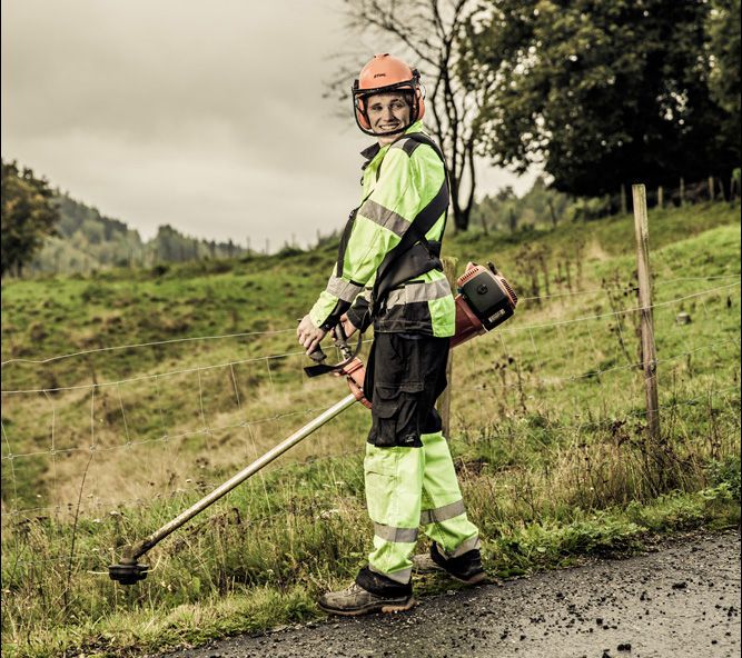 Mann med ryddesag og hjelm med visir, hørselvern og synlighetstøy. Foto.
