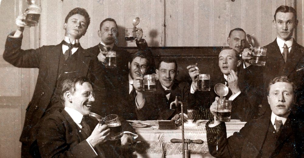 Studenter sitter rundt et bord og reiser en skål med ølglass. Foto.