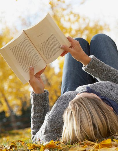 Ei kvinne ligger ute på en plen og leser ei bok. Foto.