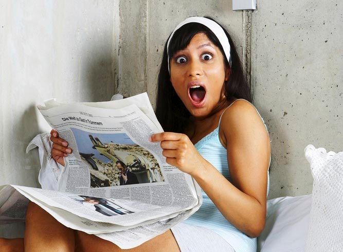 Ung kvinne holder ei avis og ser sjokkert mot kamera. Foto.