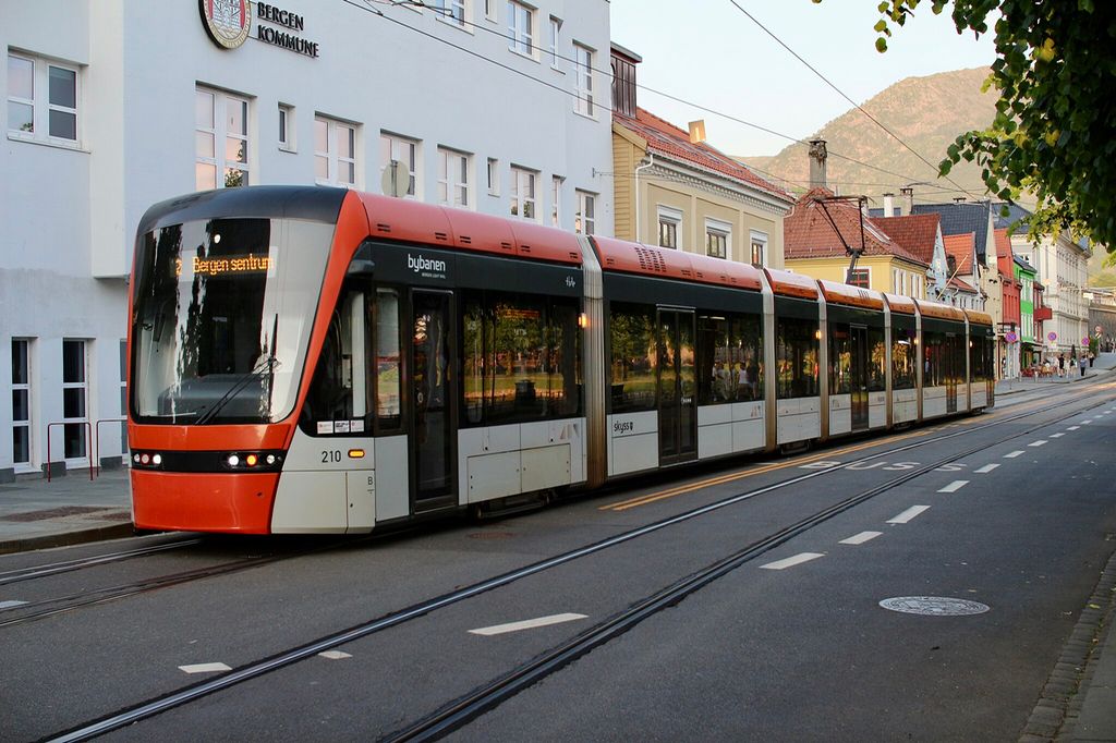 Bybanen i ei gate med stort sett eldre hus. På fasaden på en moderne bygning står det "Bergen kommune". Foto.
