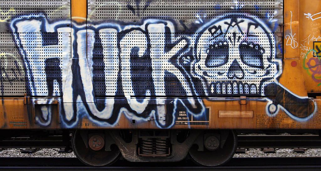 Graffiti på ei togvogn. Det står "HUCK" med store bokstaver ved siden av en hodeskalle. I panna på hodeskallen står det "SAC". Foto.