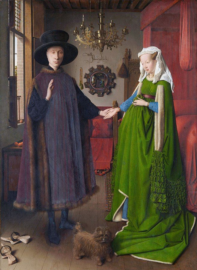 A wedding portrait from 1434. The couple is holding hands. They are dressed in expensive and colourful garments. There is a small dog on the floor between them. The room is filled with items showing that this is a rich couple. Painting.