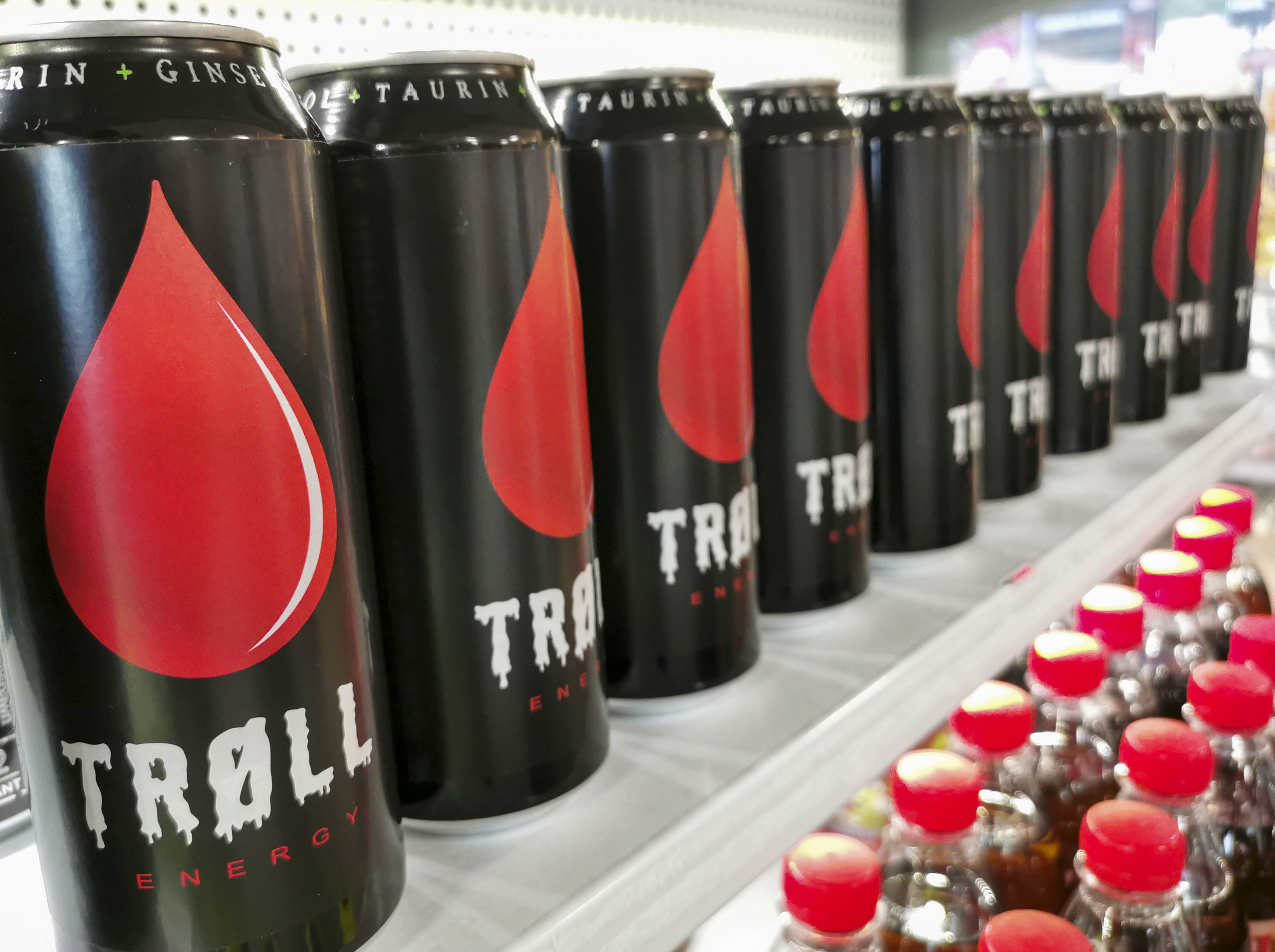 Ei rekke svarte drikkebokser på ei hylle. På boksene står det Trøll med hvit skrift under en dråpeformet rød logo. Foto.