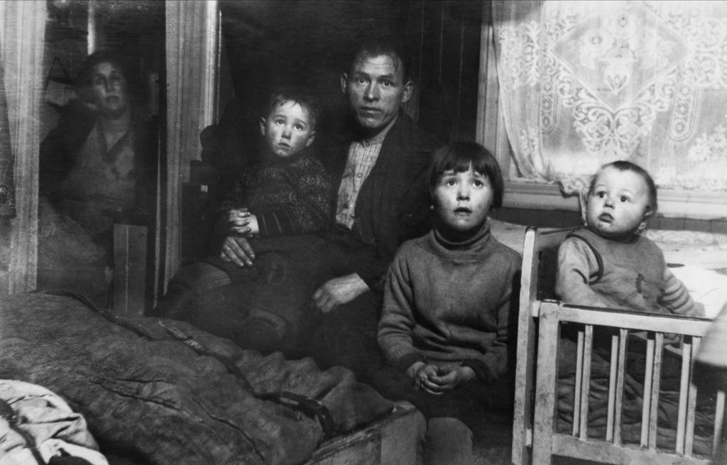 En familie på to voksne og tre barn i et trangt soverom, ca. 1930. Foto.