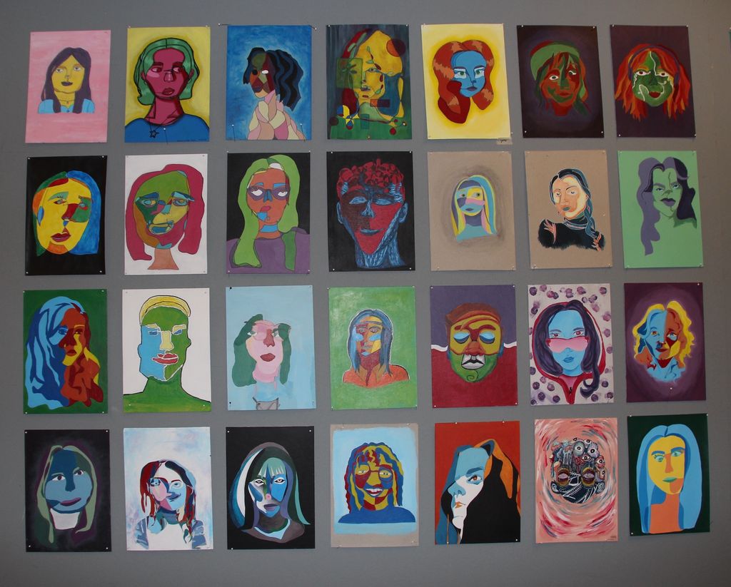 En vegg med mange fargerike selvportretter laget med blindkontur. Foto.