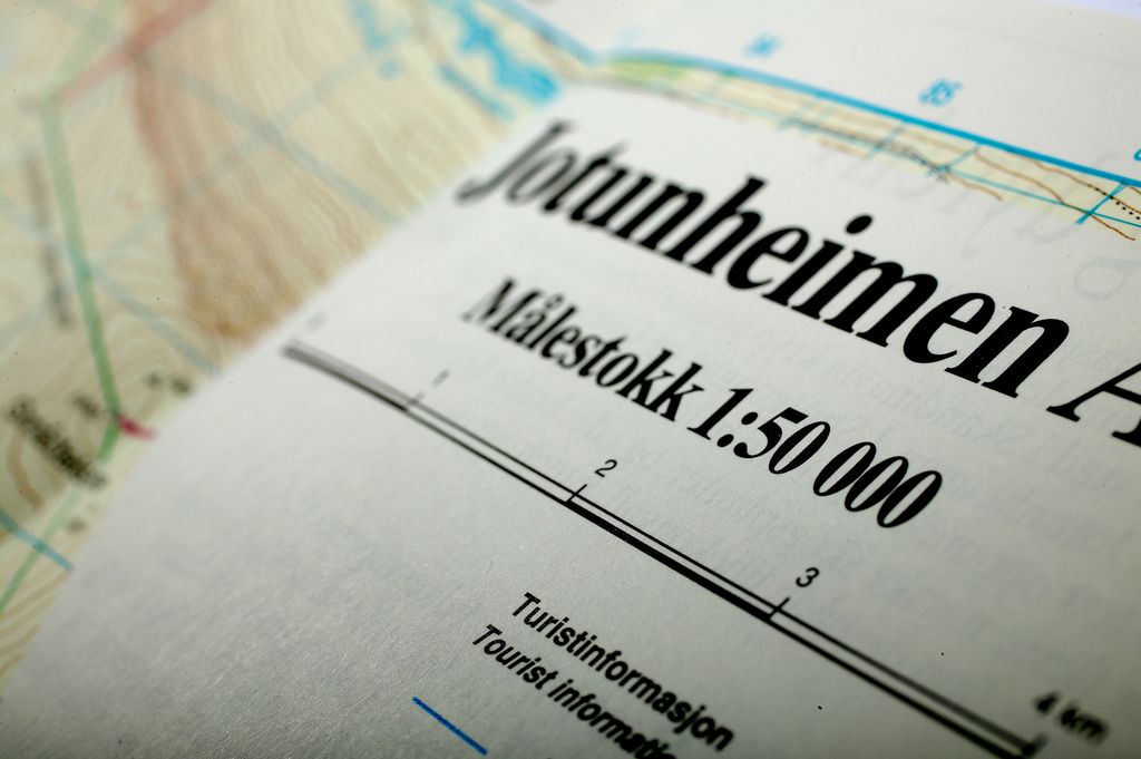 Nærbilde av en side i ei kartbok. Siden har overskriften Jotunheimen. Under står det målestokk 1 til 50000. I utkanten av bildet skimtes høydekoter og andre linjer på et topografisk kart. Foto.