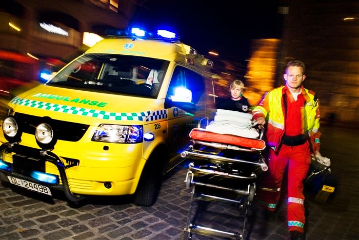 En ambulanse med blålys og paramedicer som løper med båra. Foto.