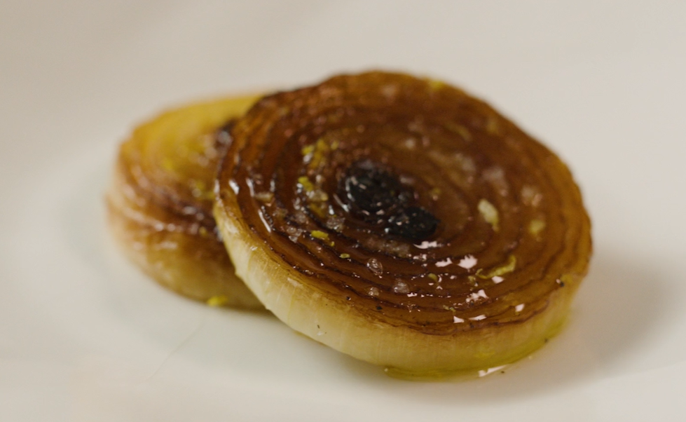 To skiver med karamellisert løk anrettet på en hvit tallerken. Foto.