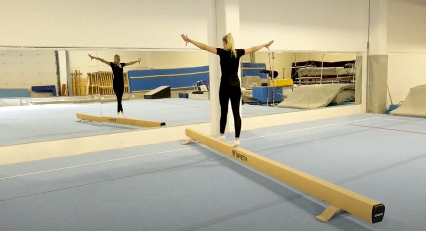 Jente som balanserer på en bom med armene ut til siden. Foto.