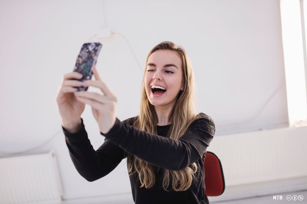 En kvinne smiler og blunker med øye mens hun tar en selfie. Foto.