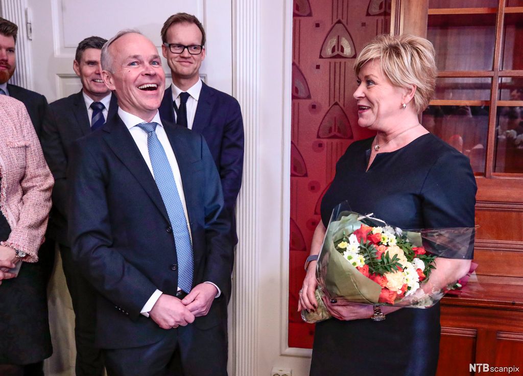 Mann og kvinne snakker sammen og ler. Kvinnen holder bukett med blomster. Foto.
