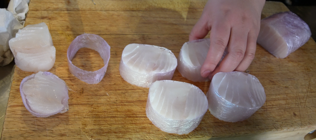 Skreifilet som er rullet stramt i plast til ei pølse, kuttes opp i serveringsstykker. Foto.