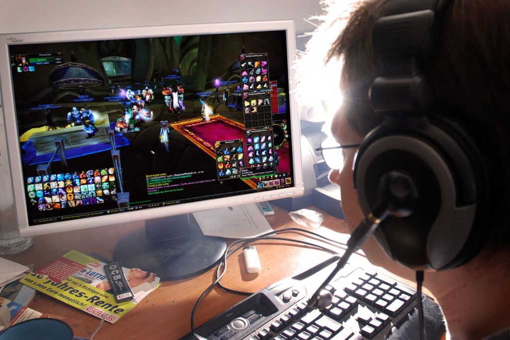 Ung mann sit framfor ein stor dataskjerm og speler videospel. Foto.