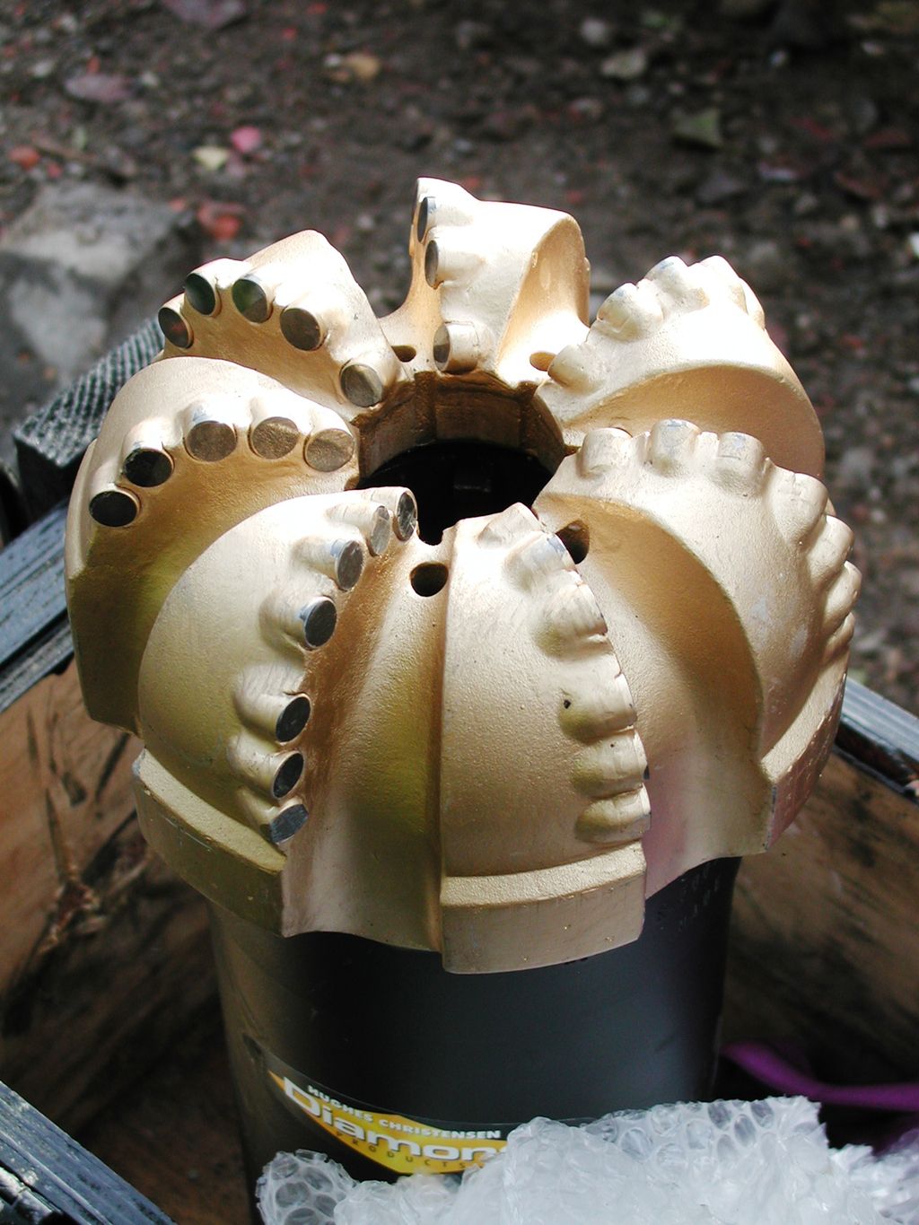 Borekrone for brønnboring, med små biter av kunstig diamant innsatt i kutteflaten. Denne borekronen brukes til å kutte gjennom bergarten. Foto.