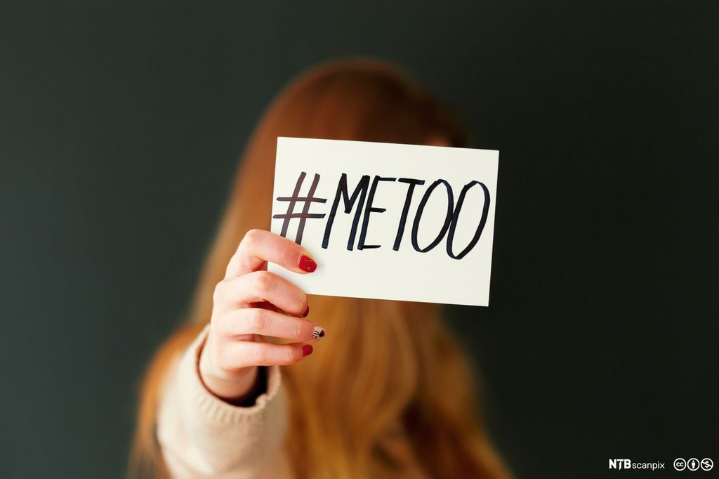 En rødhåret kvinne holder opp et ark med teksten emneknagg METOO. Foto.