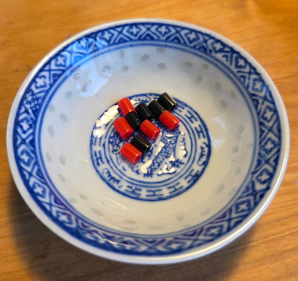 Fem svarte og fem raude perler i ei porselensskål. Foto.