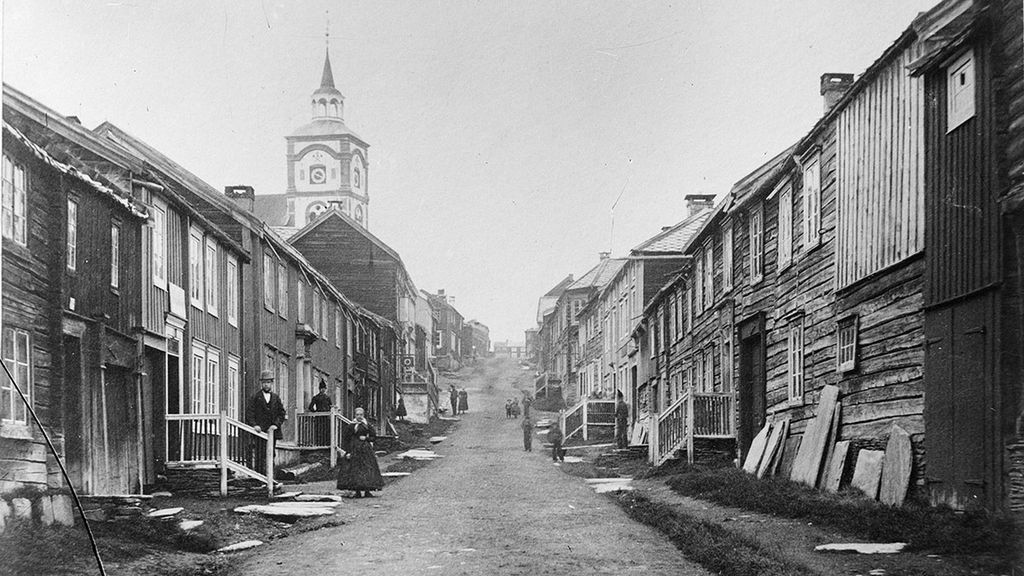 Bygate i Røros med mennesker både i forkant og bakkant. Kirken kan ses bakerst til venstre. Foto.