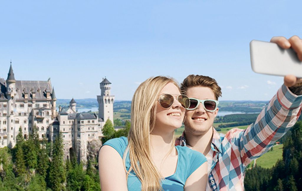 To unge personer tar en selfie foran slottet Neuschwanstein. Foto.