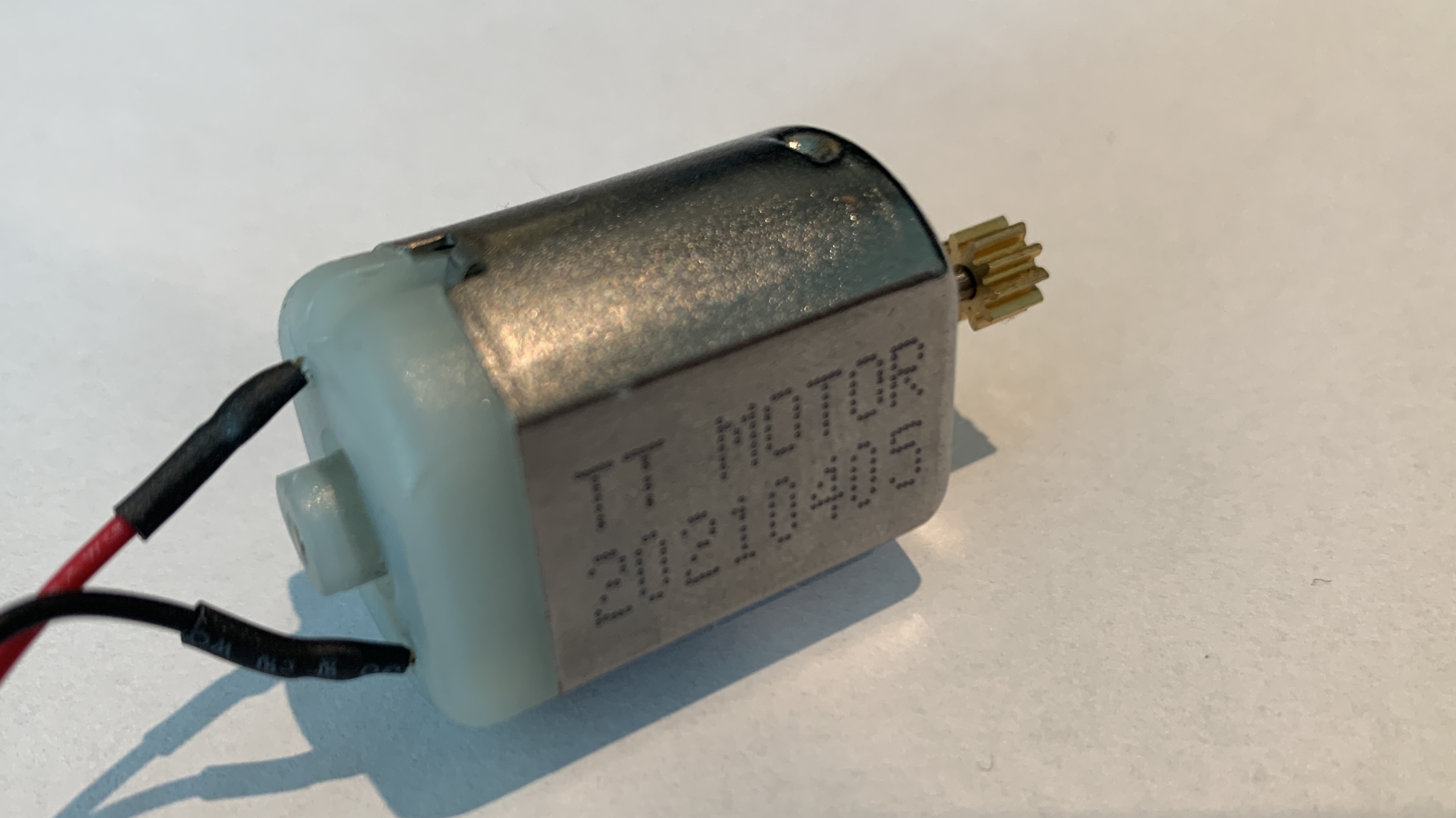 DC-motor. En liten firkant i metall og plast, med to ledninger i den ene enden og en tannhjulsforma skrue i motsatt ende. Foto.